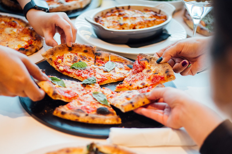 Deux personnes prennent des morceaux de pizza dans un plateau.